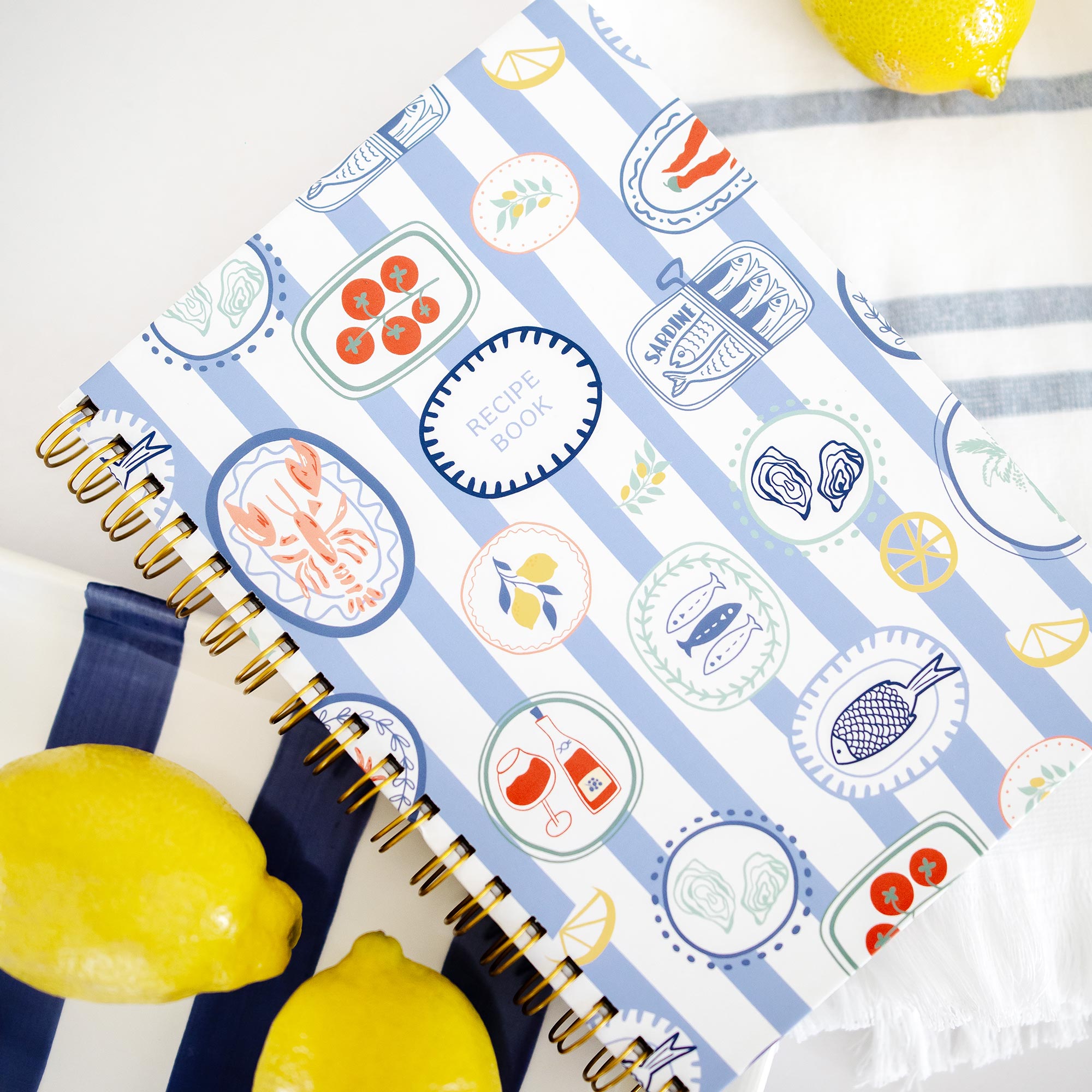 Angled view of a personalized recipe book with blue and white stripe cover and gold spiral binding