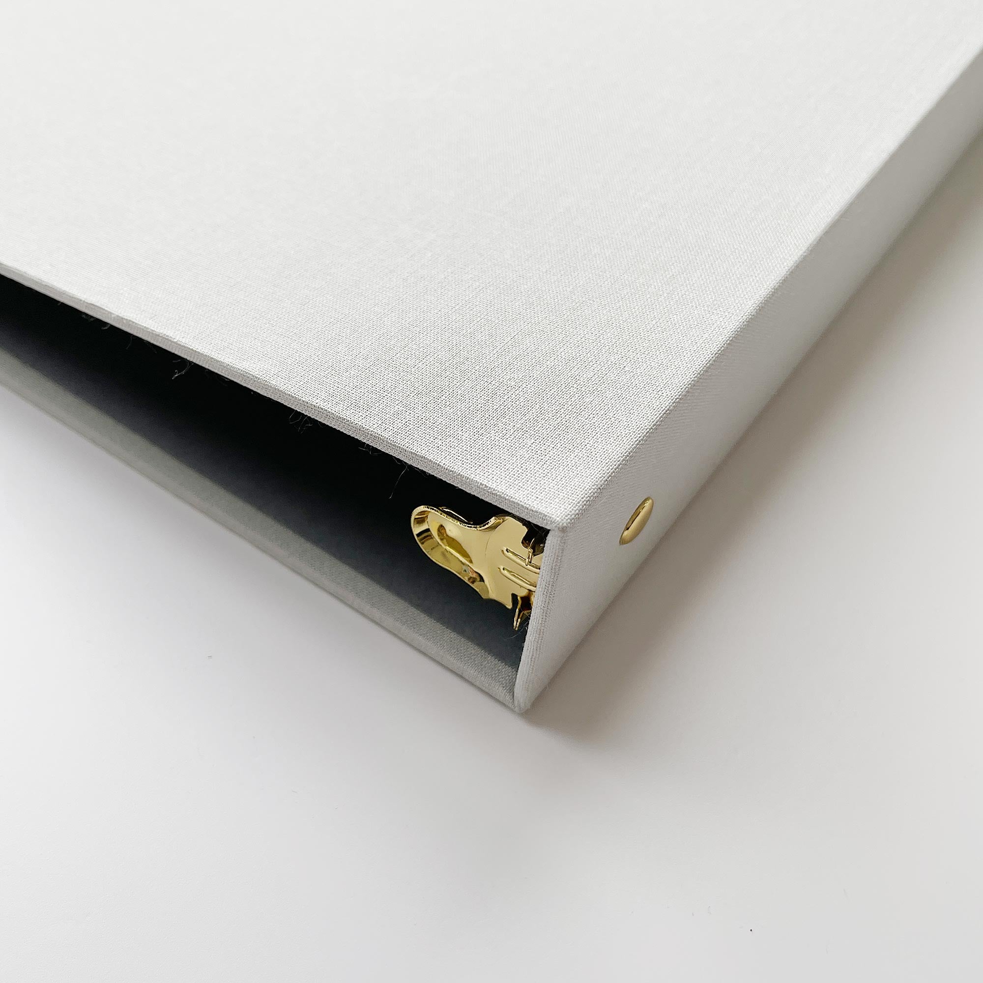 Angled view of a beige linen binder with gold hardware on a white background