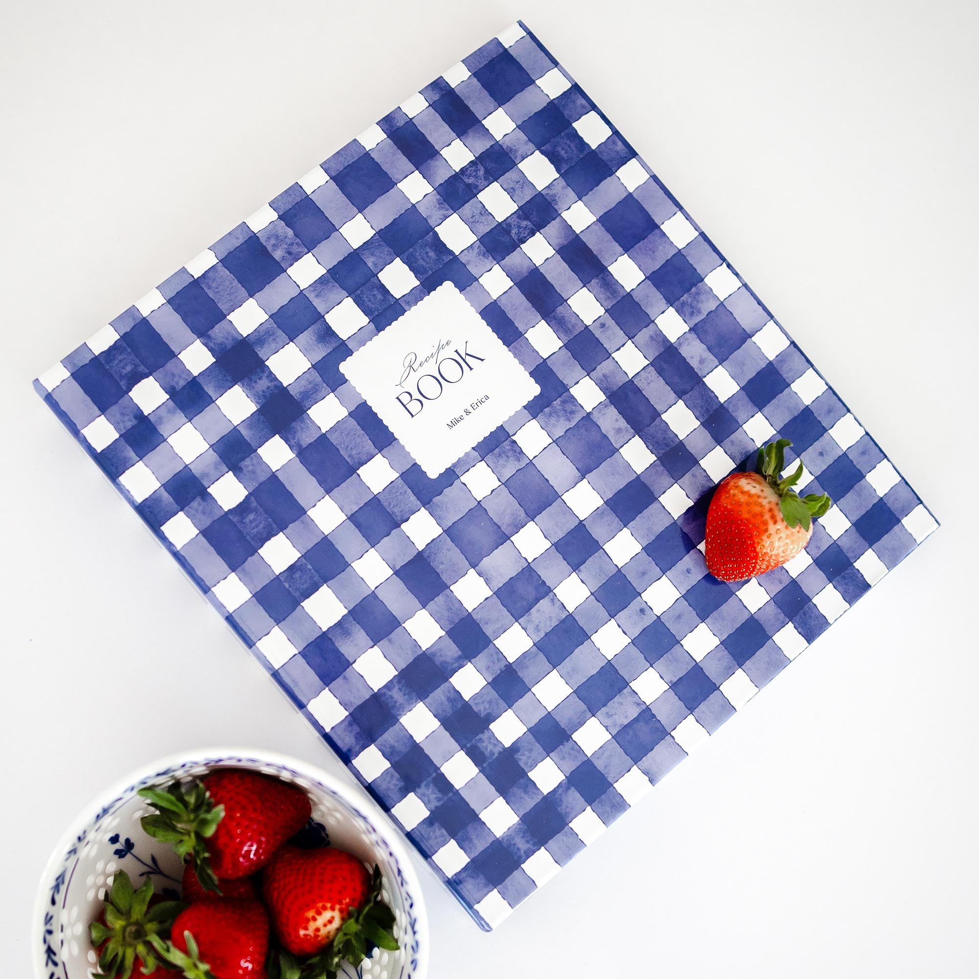 Styled flatlay featuring a Keepsake Paper Co. blue and white gingham recipe binder on a white background with strawberries