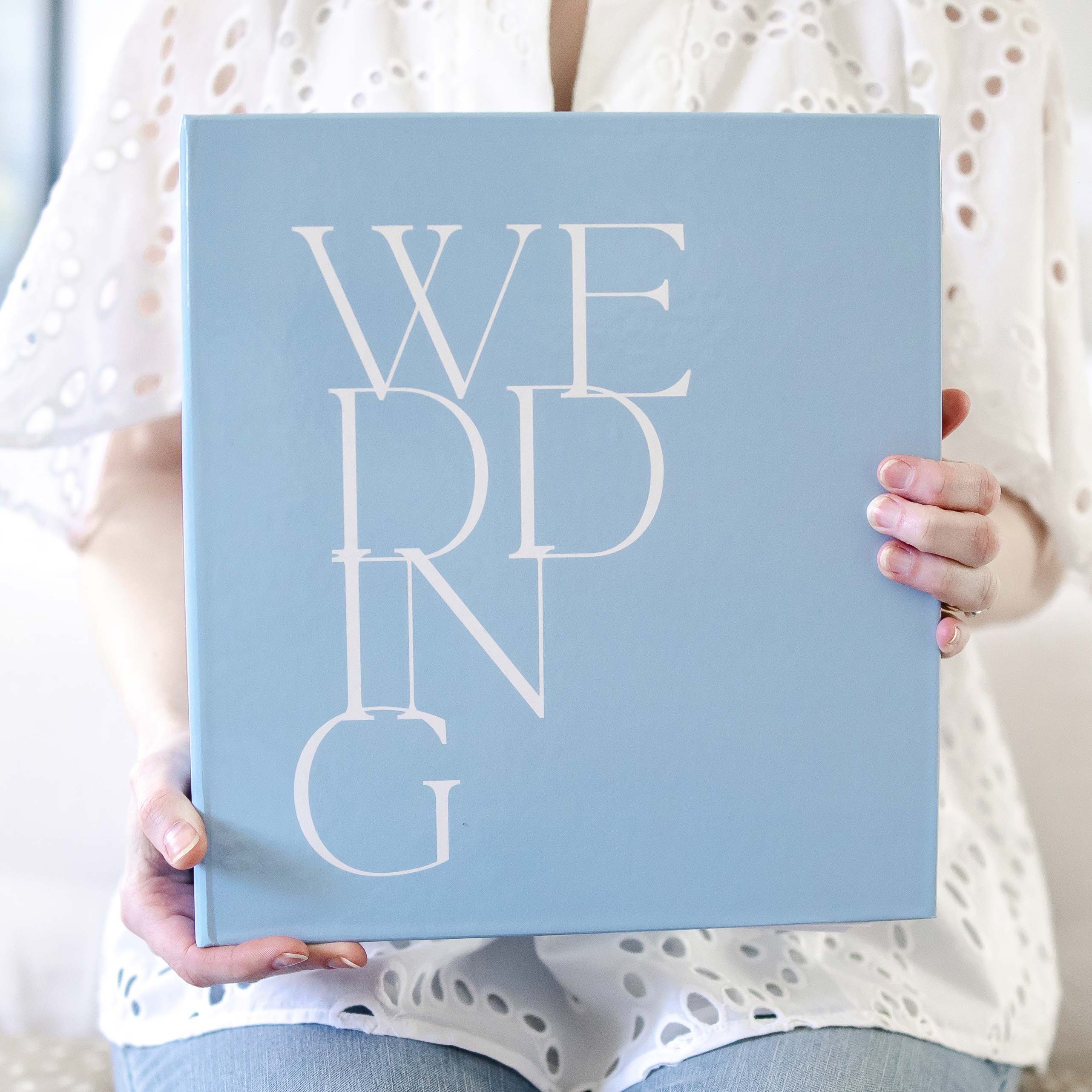 Styled image featuring a women holding a Keepsake Paper Co. LGBT wedding binder with white text and a blue cover