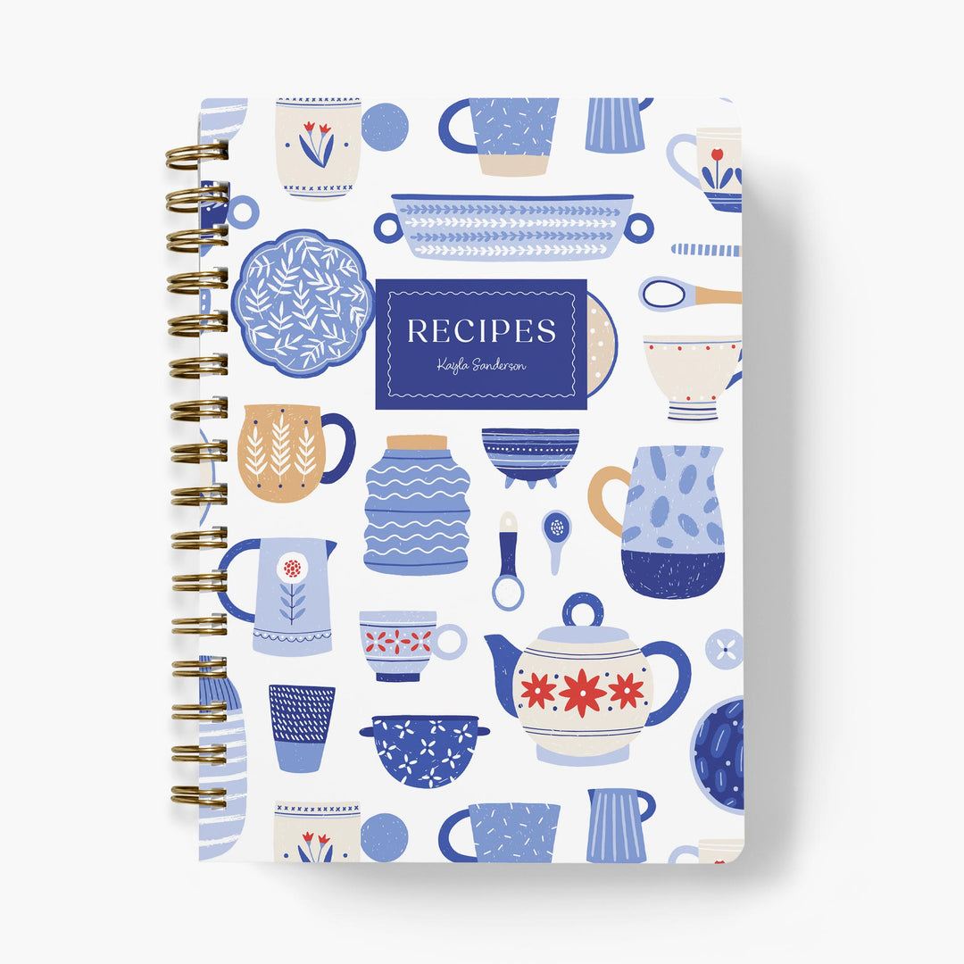 Custom recipe journal with a blue and white dishware pattern with gold binding on a white background
