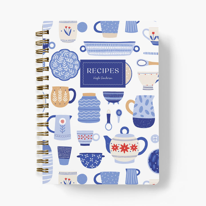 Custom recipe journal with a blue and white dishware pattern with gold binding on a white background
