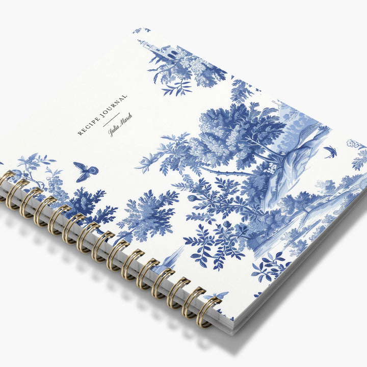Custom cookbook in a French toile pattern on a white background with brass binding
