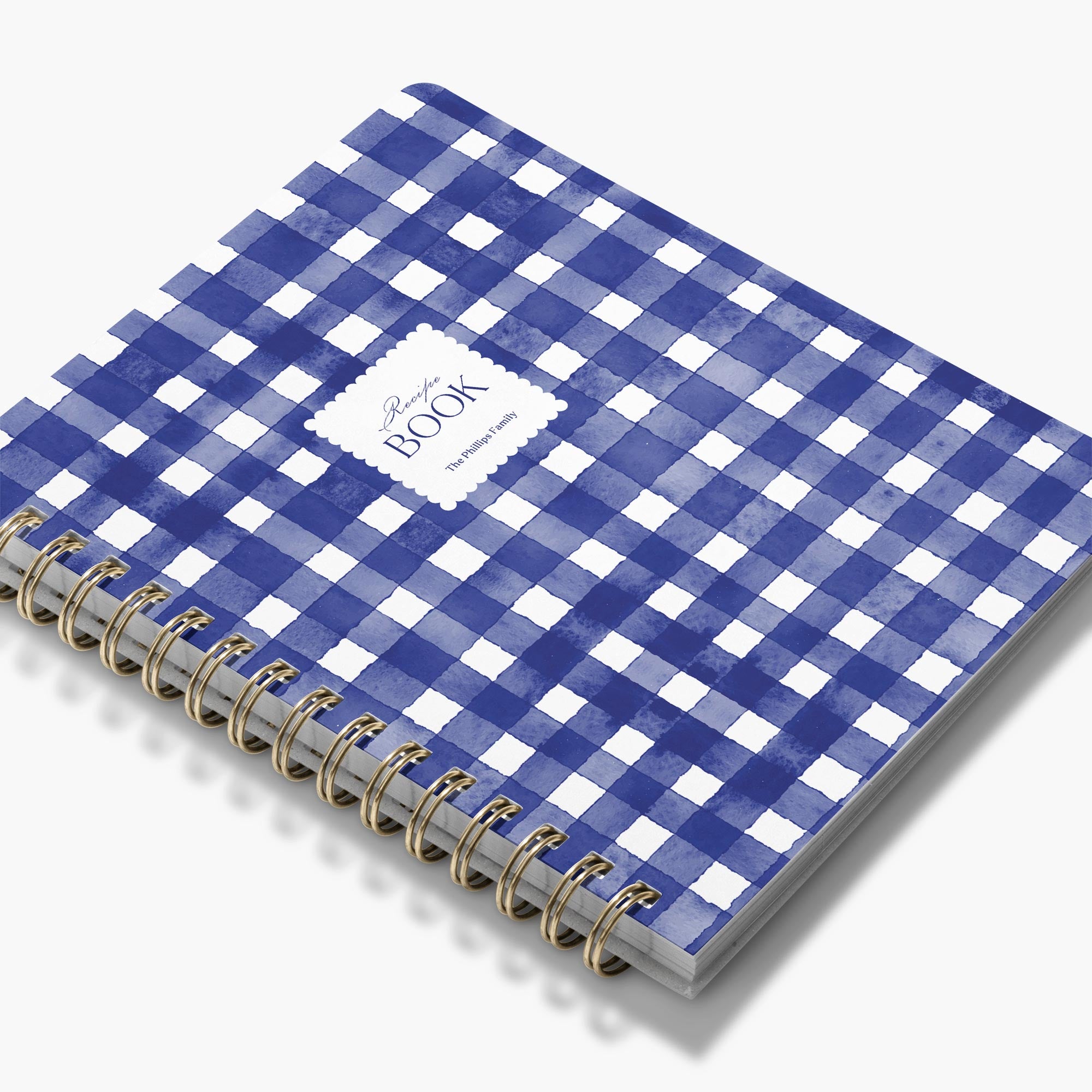 Custom cookbook in a blue and white checkered pattern with gold spiral binding on a white background
