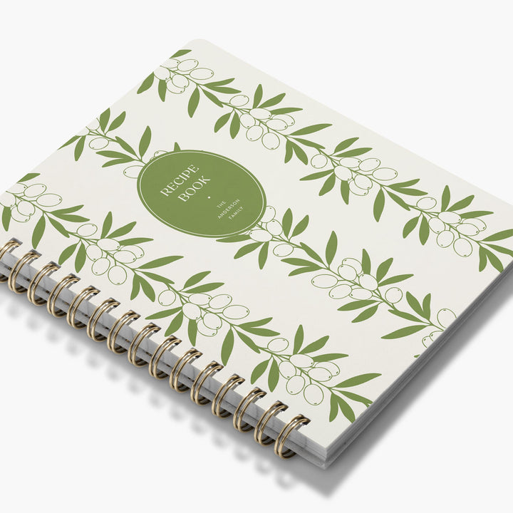 Custom cookbook with green olive leaves bound in gold wire on a white background