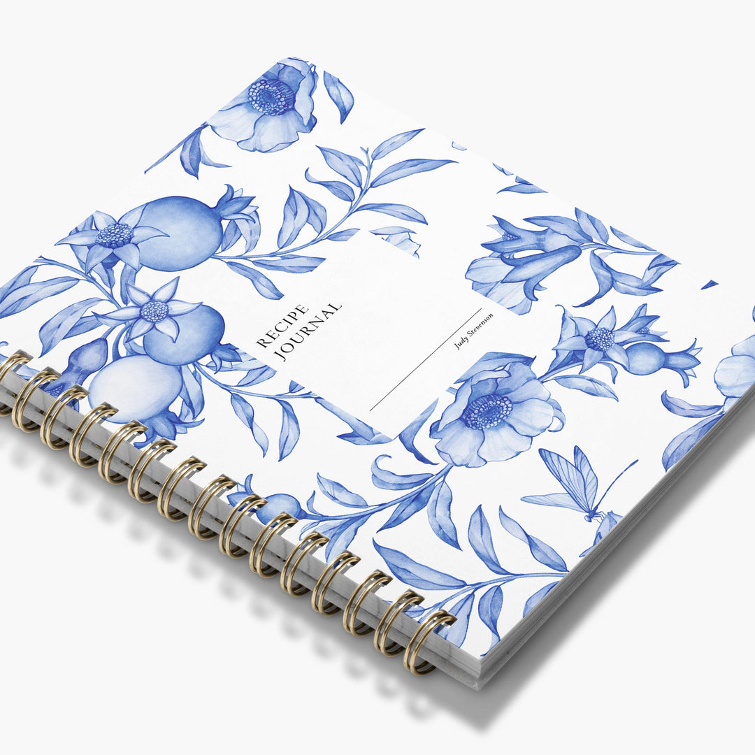 Custom cookbook with blue and white floral design and gold spiral binding on a white background