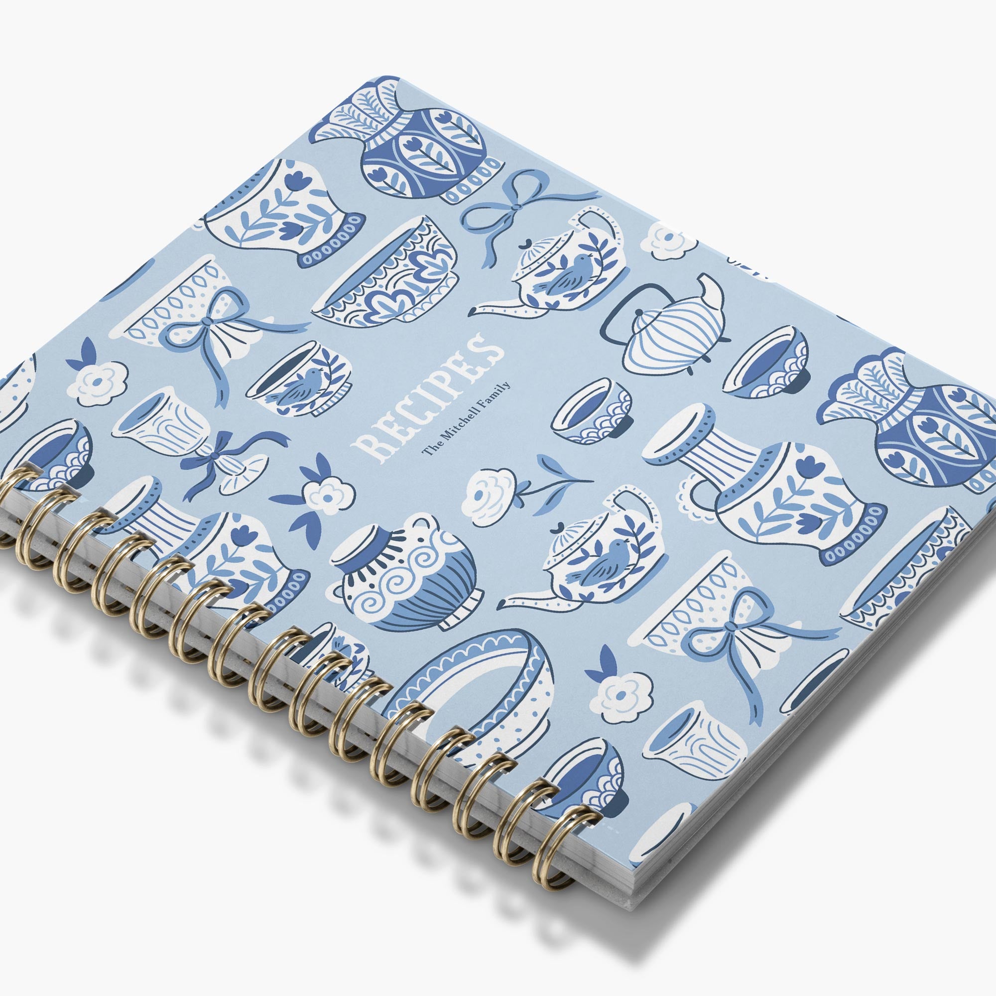 Angled view of a personalized recipe book with a pattern of blue and white dishes on the cover.