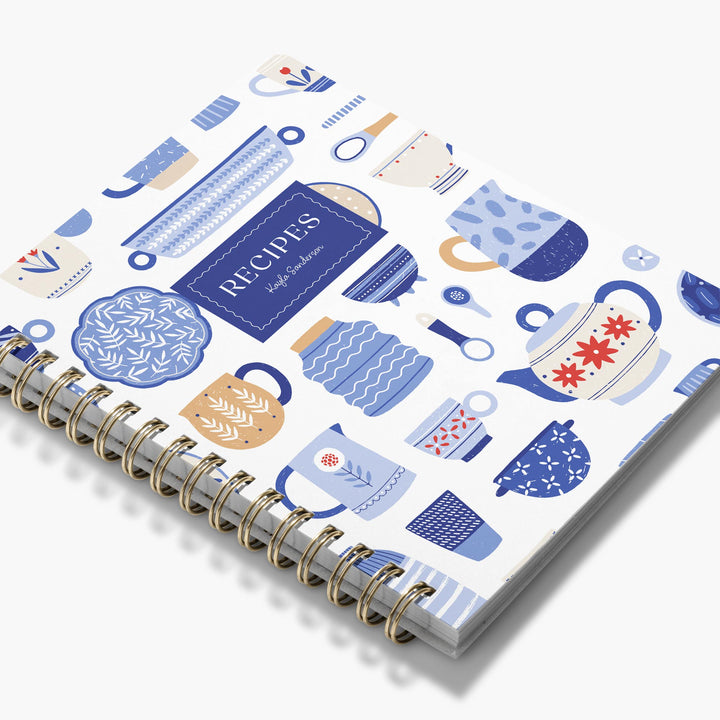 Custom cookbook with blue and white teapots and dishes on a white background