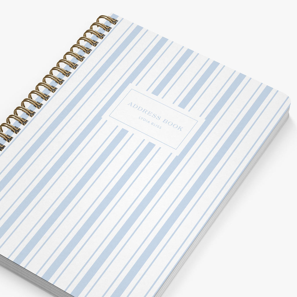 Notebook with blue and white striped cover and gold spiral binding on a white background
