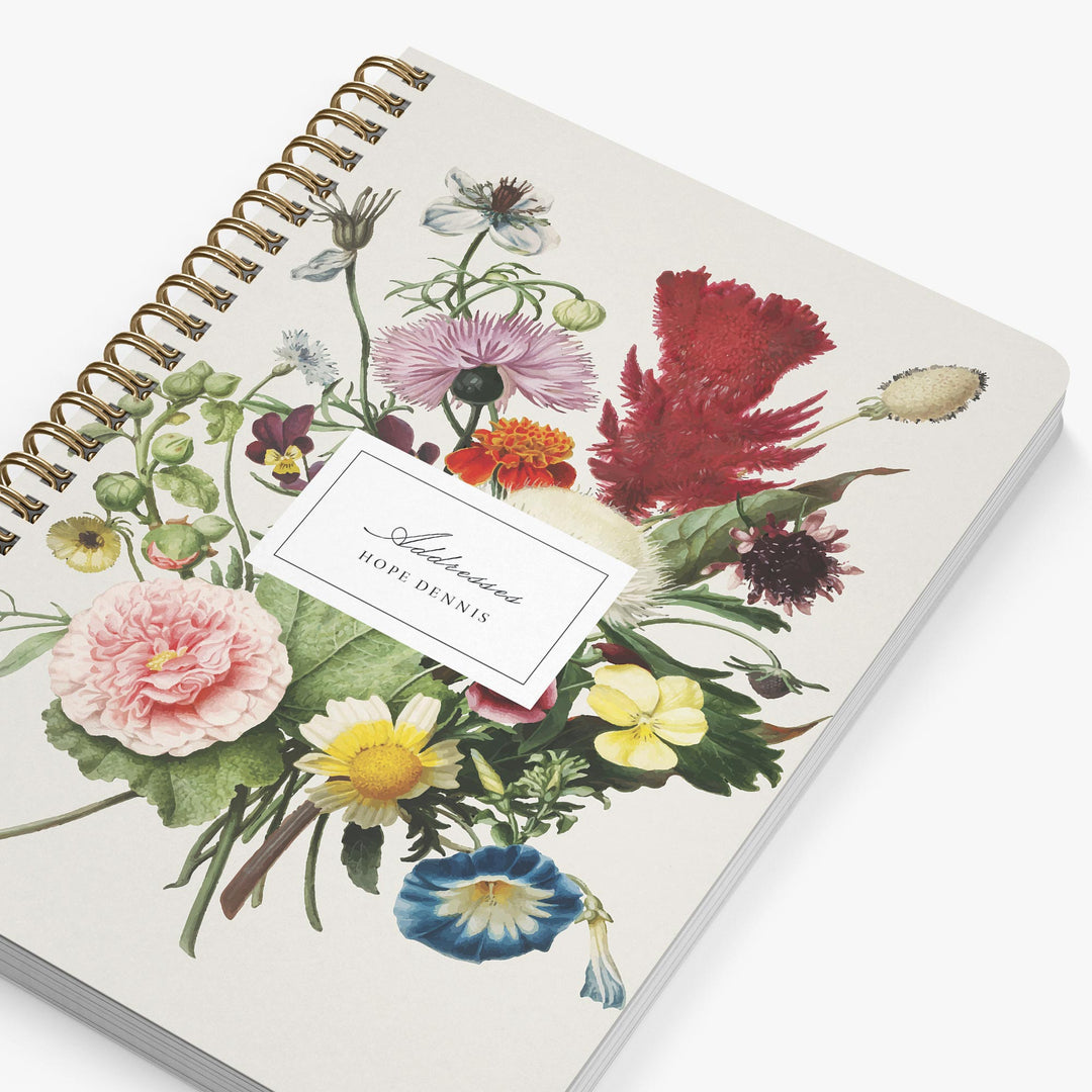 Notebook with floral design and gold spiral binding on a white background