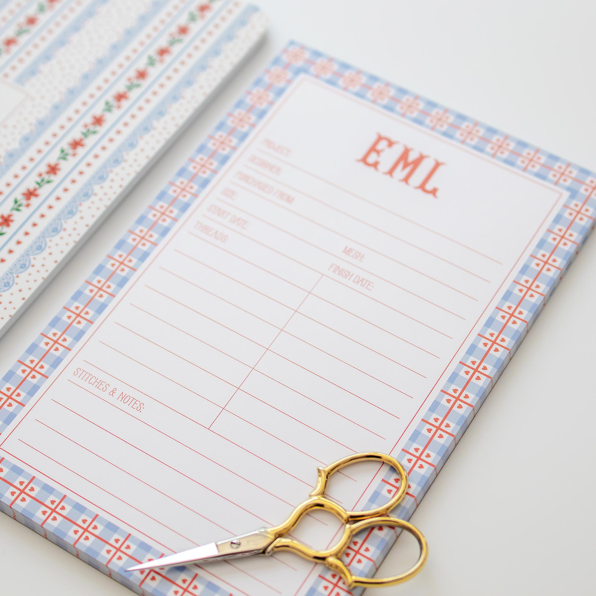 Needlepoint notepad with gingham heart border and personalization, accompanied by gold scissors on a light background