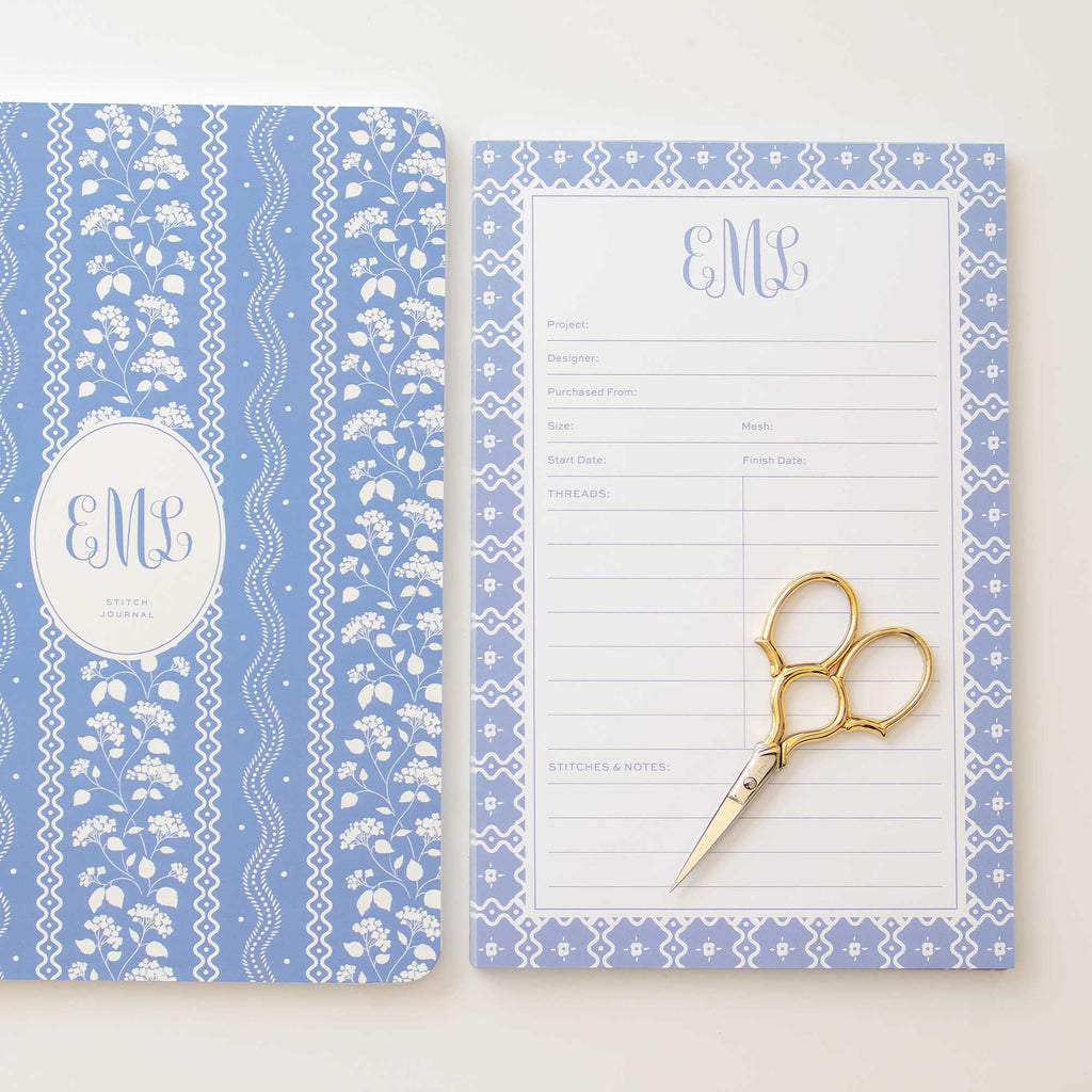 Custom needlepoint notepad and tracking journal shown side by side styled with a pair of gold gingher scissors