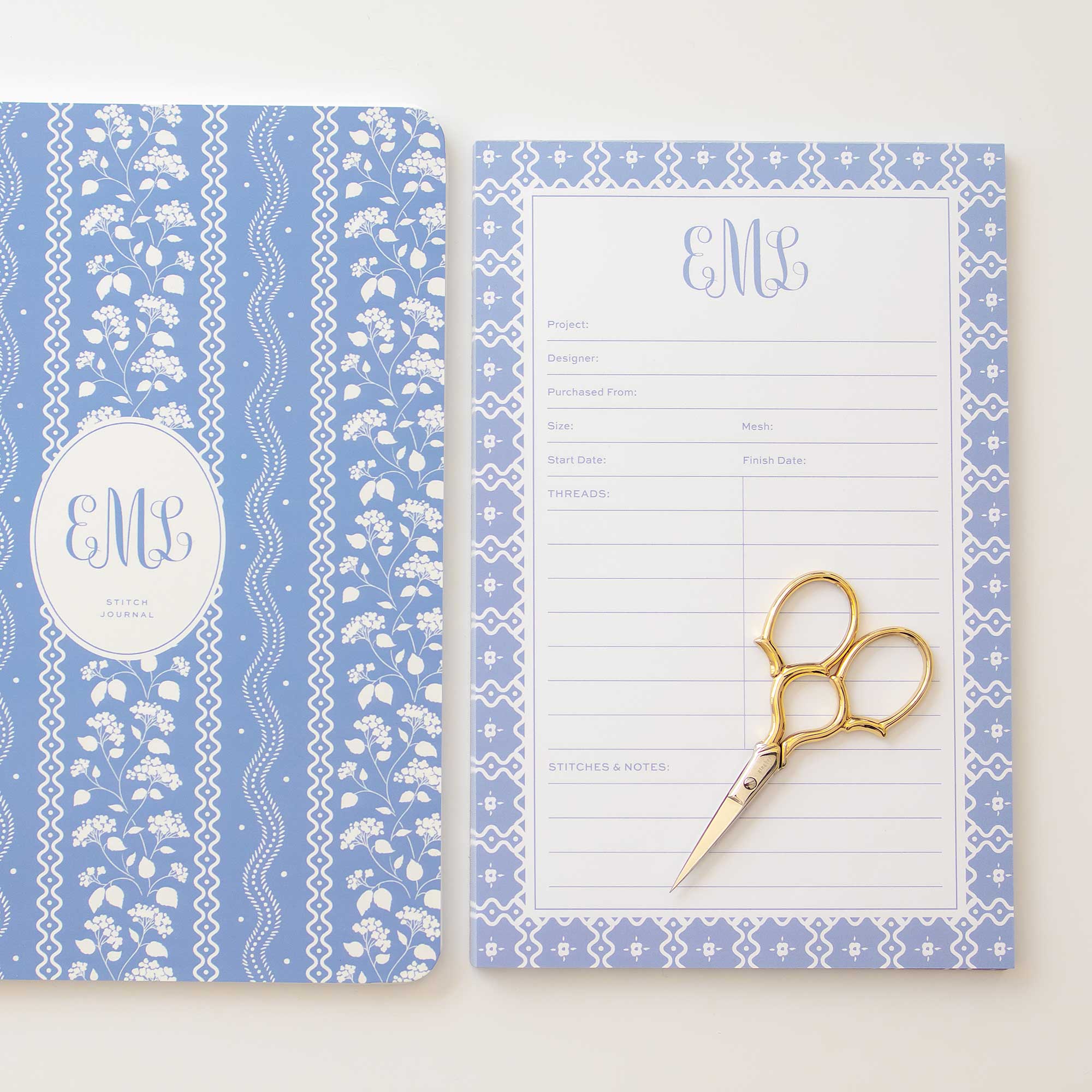 Custom needlepoint notepad and tracking journal shown side by side styled with a pair of gold gingher scissors