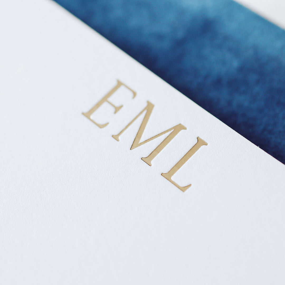 Closeup of gold foil monogram printed on cotton paper on a blue velvet notebook