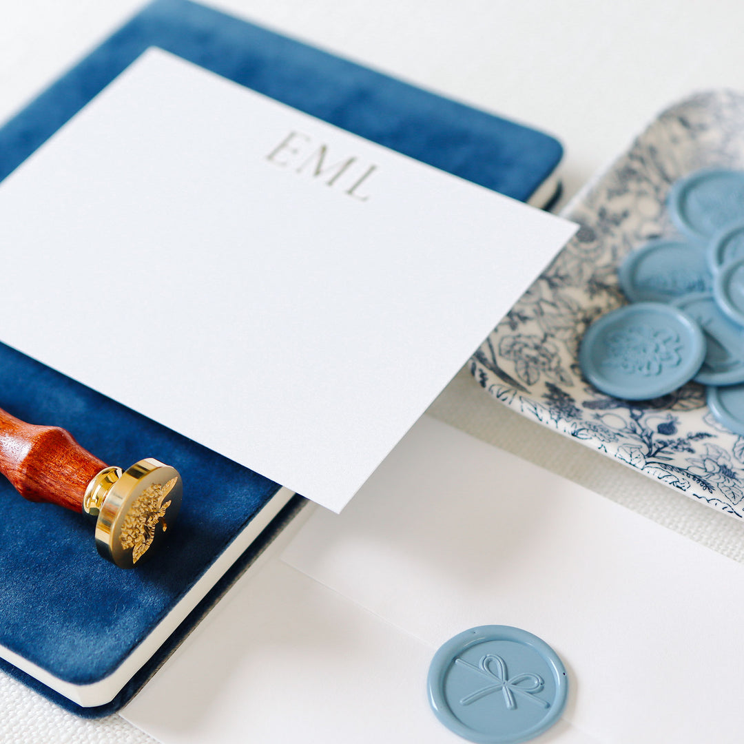 Detail shot of grand monogram design notecard with white cotton envelope styled with wax seal accessories