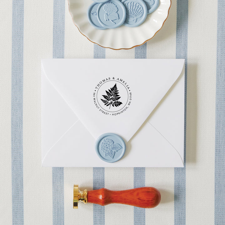 Custom fern address stamp on white envelope surrounded by wax seals and an embosser