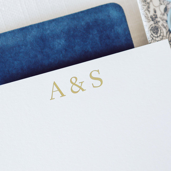Gold foil monogram note card on white cotton paper over a blue velvet notebook