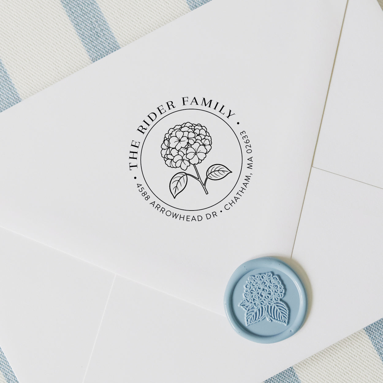 Custom hydrangea address stamp on a white envelope with wax seal and blue and white striped background
