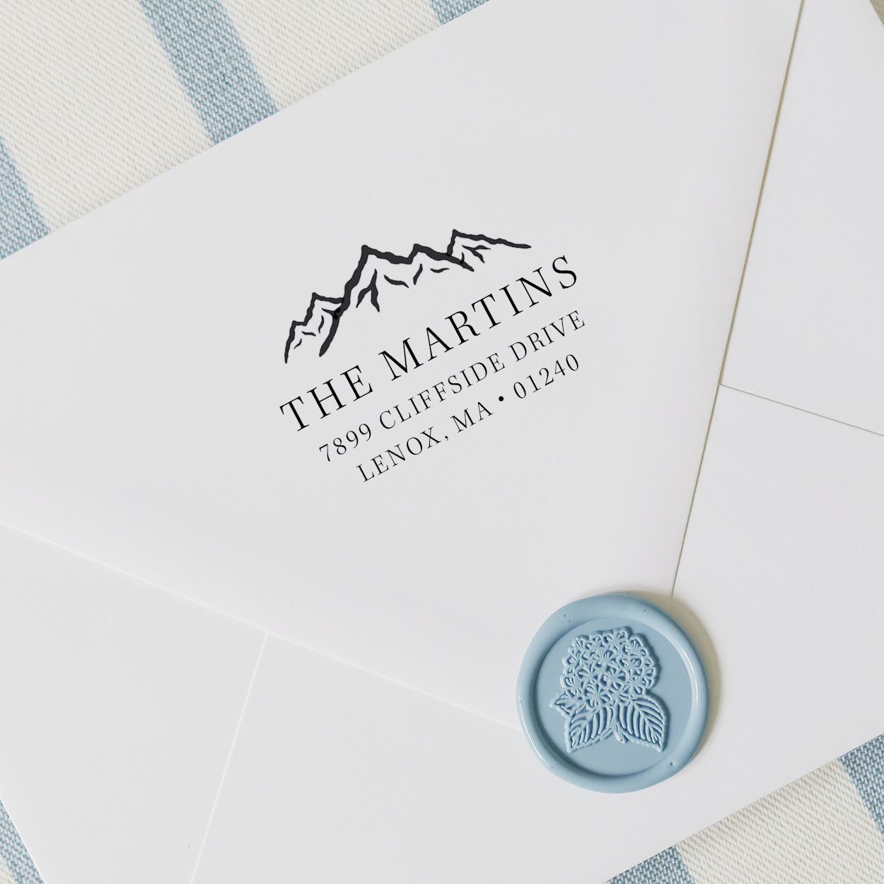 Personalized address stamp with mountain range on a white envelope with wax seal and striped background
