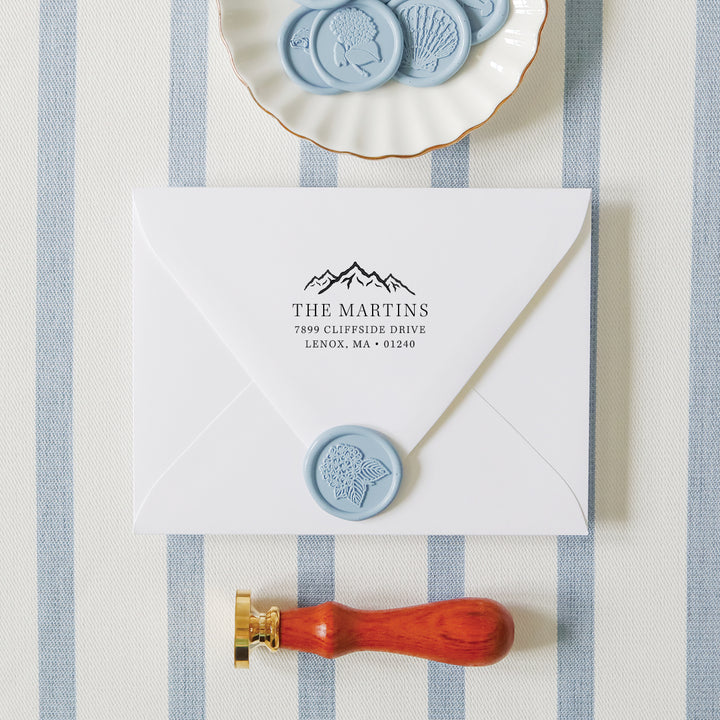 Custom return address stamp on a white envelope flanked by an embosser and dish of wax seals