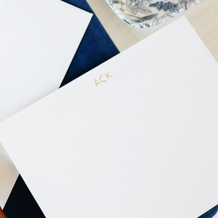 A custom gold foil notecard on white cotton paper styled with blue accessories