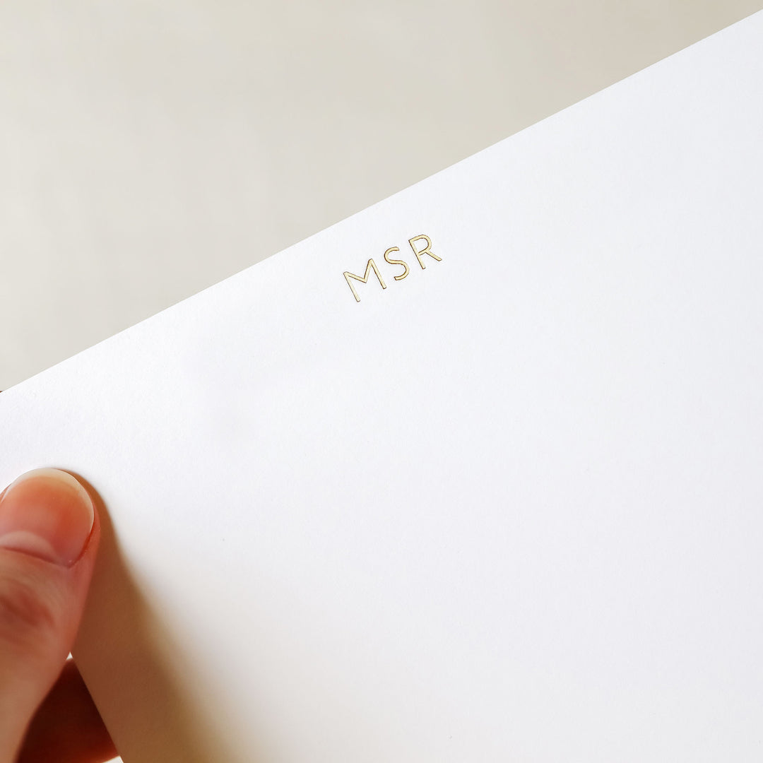 A hand holds a custom notecard that has been printed in gold foil on cotton paper