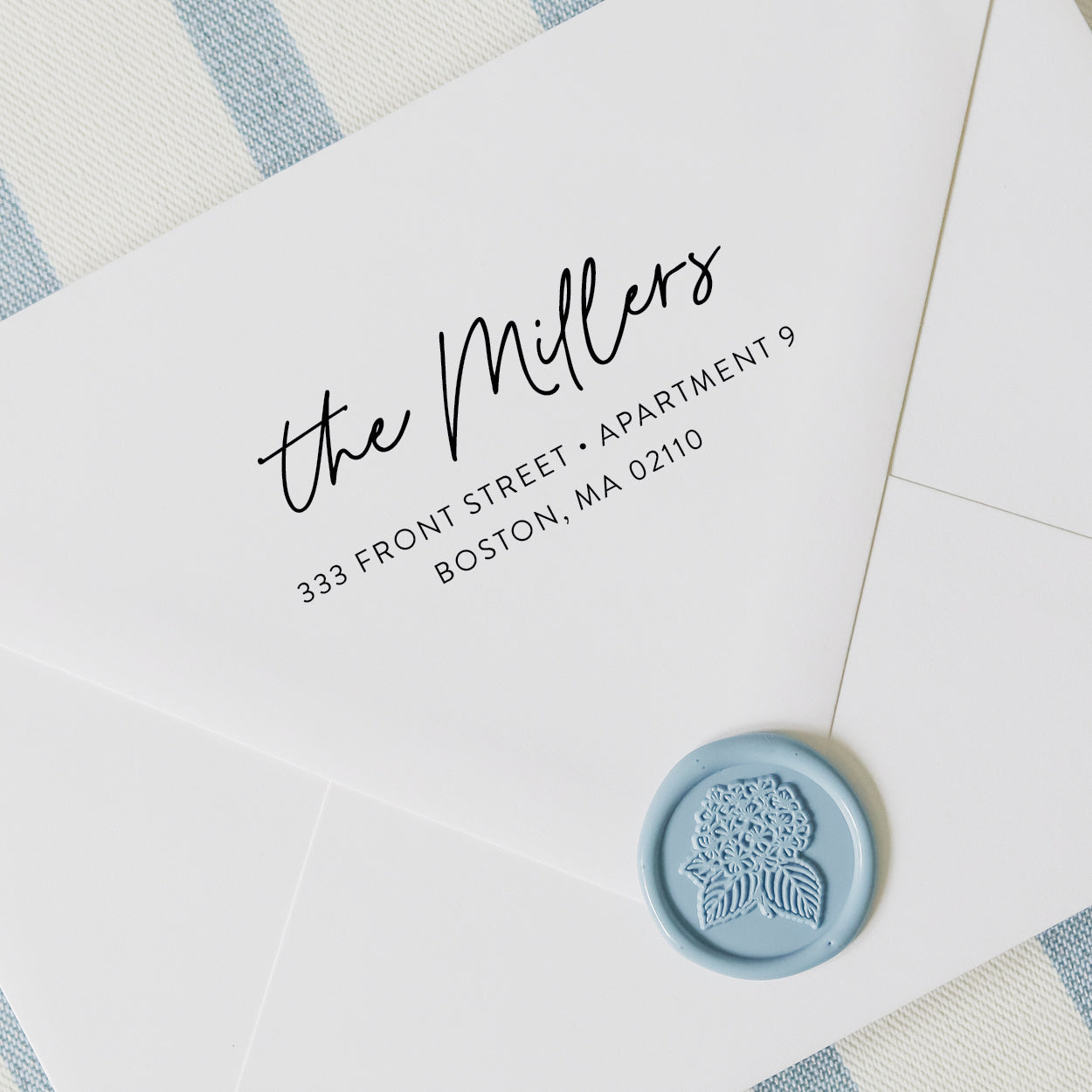 Personalized address stamp with modern script design on a white envelope with blue wax seal