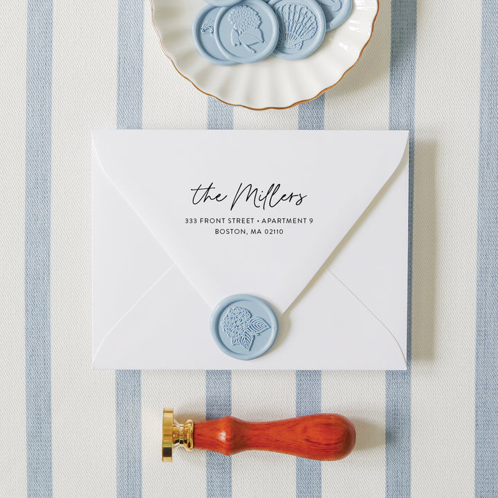 Custom return address stamp in a modern script font on a white envelope styled with floral wax seals and embosser