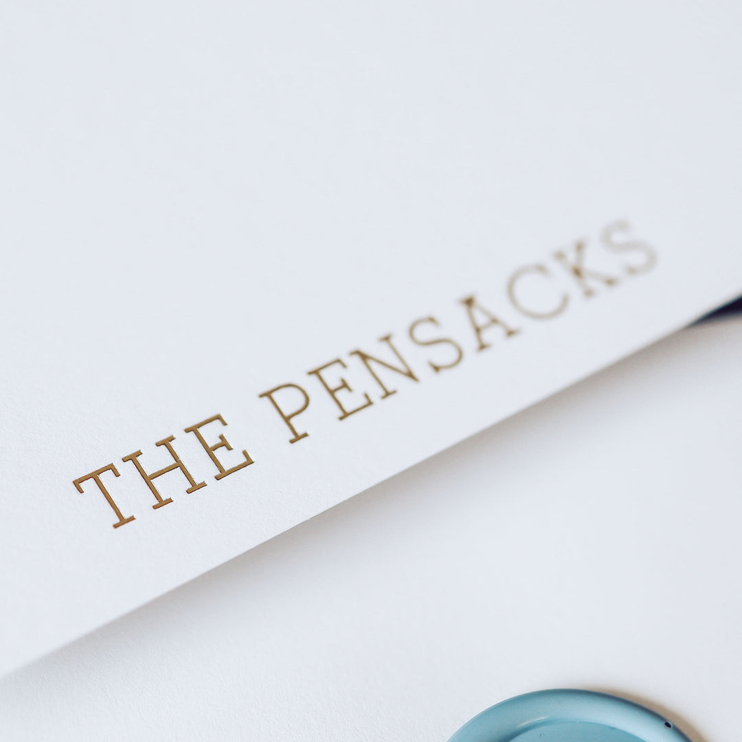 A closeup of gold foil lettering that has been printed on a white cotton note card