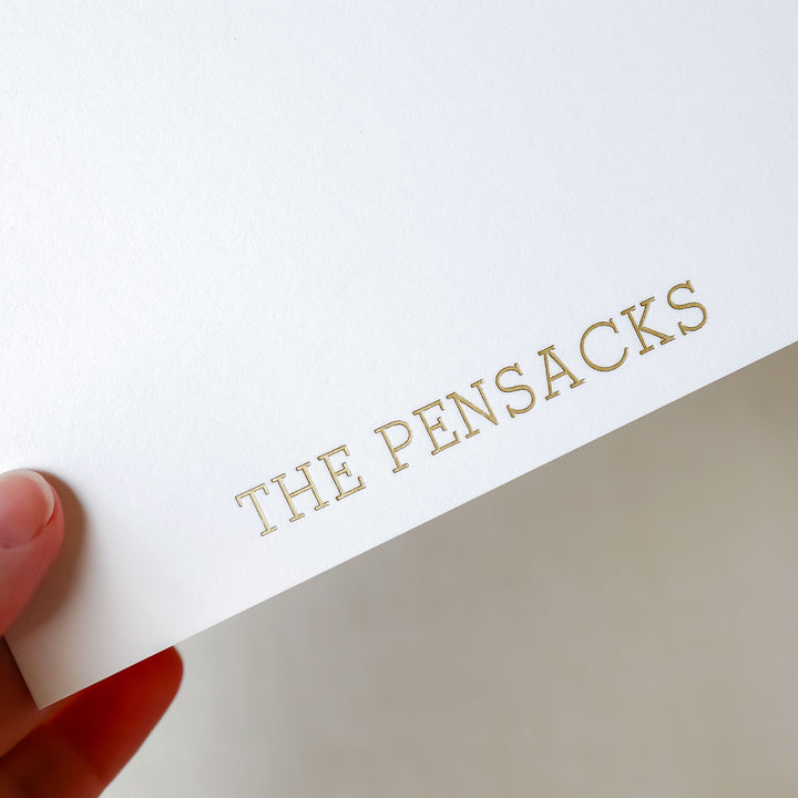 A hand holds a personalized notecard on cotton paper over a neutral background