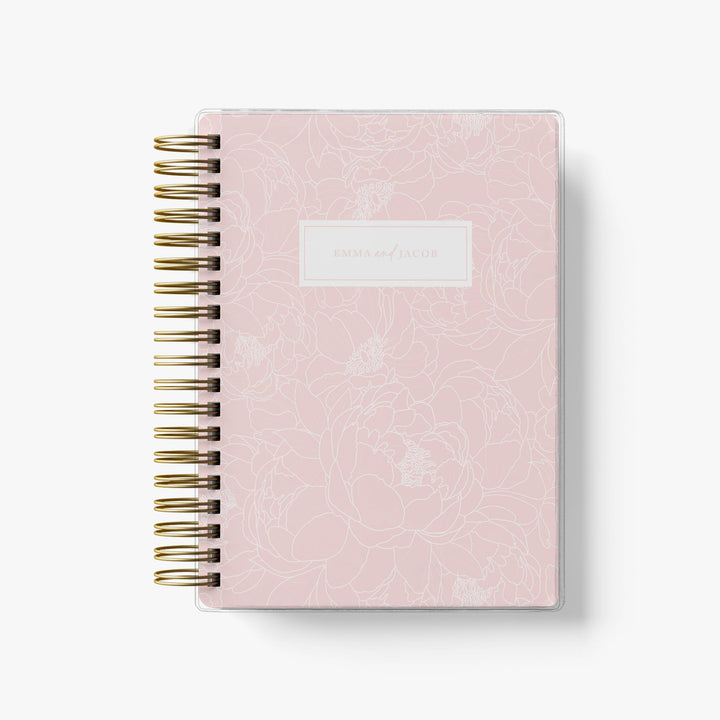 Custom wedding planner featuring a floral, blush pink peony cover that is personalized with the names of the couple