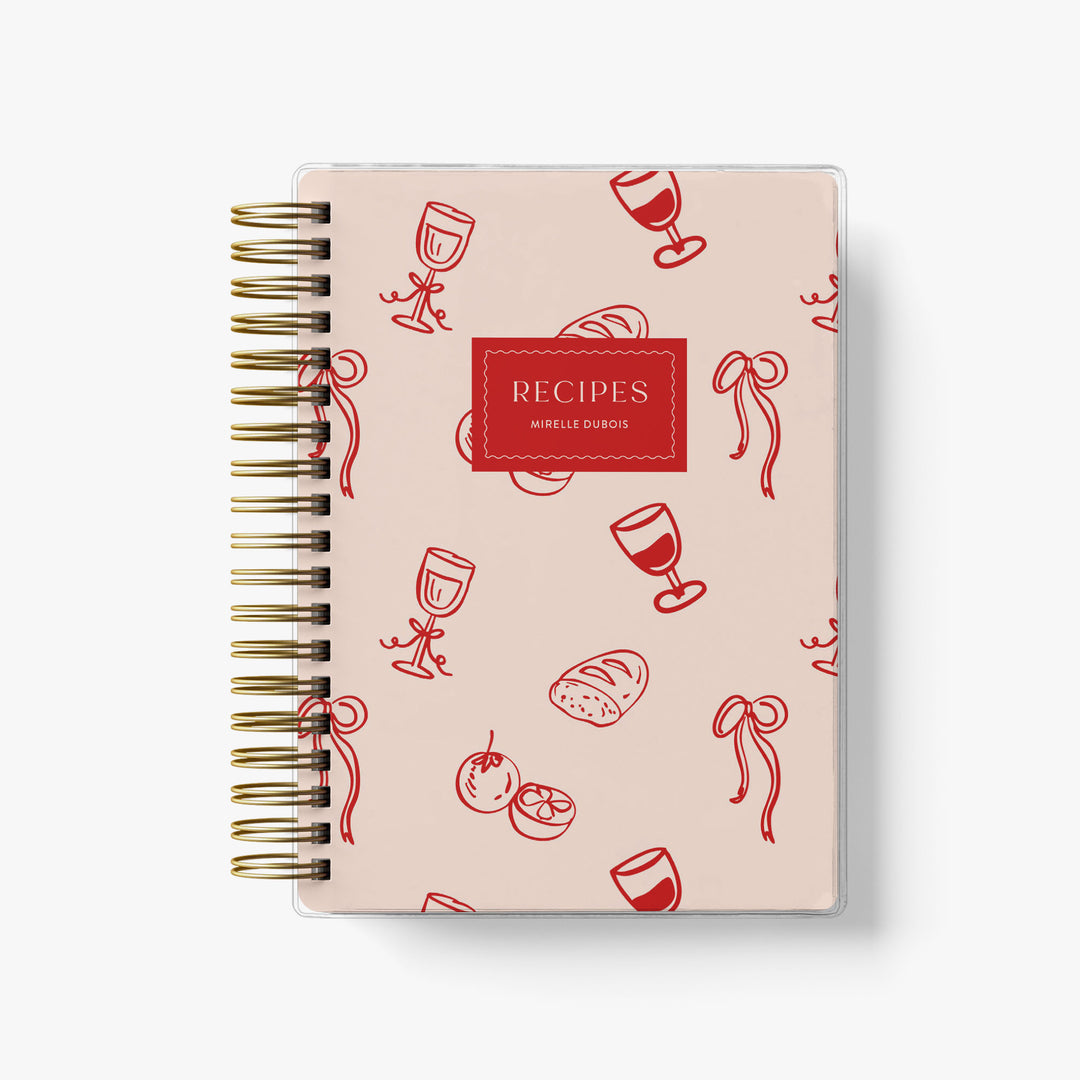 This French-inspired custom recipe journal features an adorable pink and red pattern with bows, wine and bread