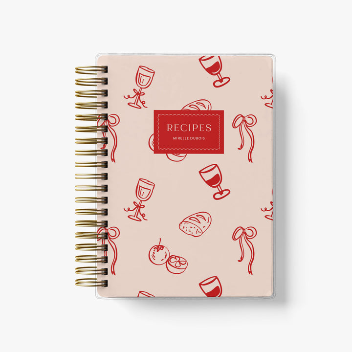 This French-inspired custom recipe journal features an adorable pink and red pattern with bows, wine and bread