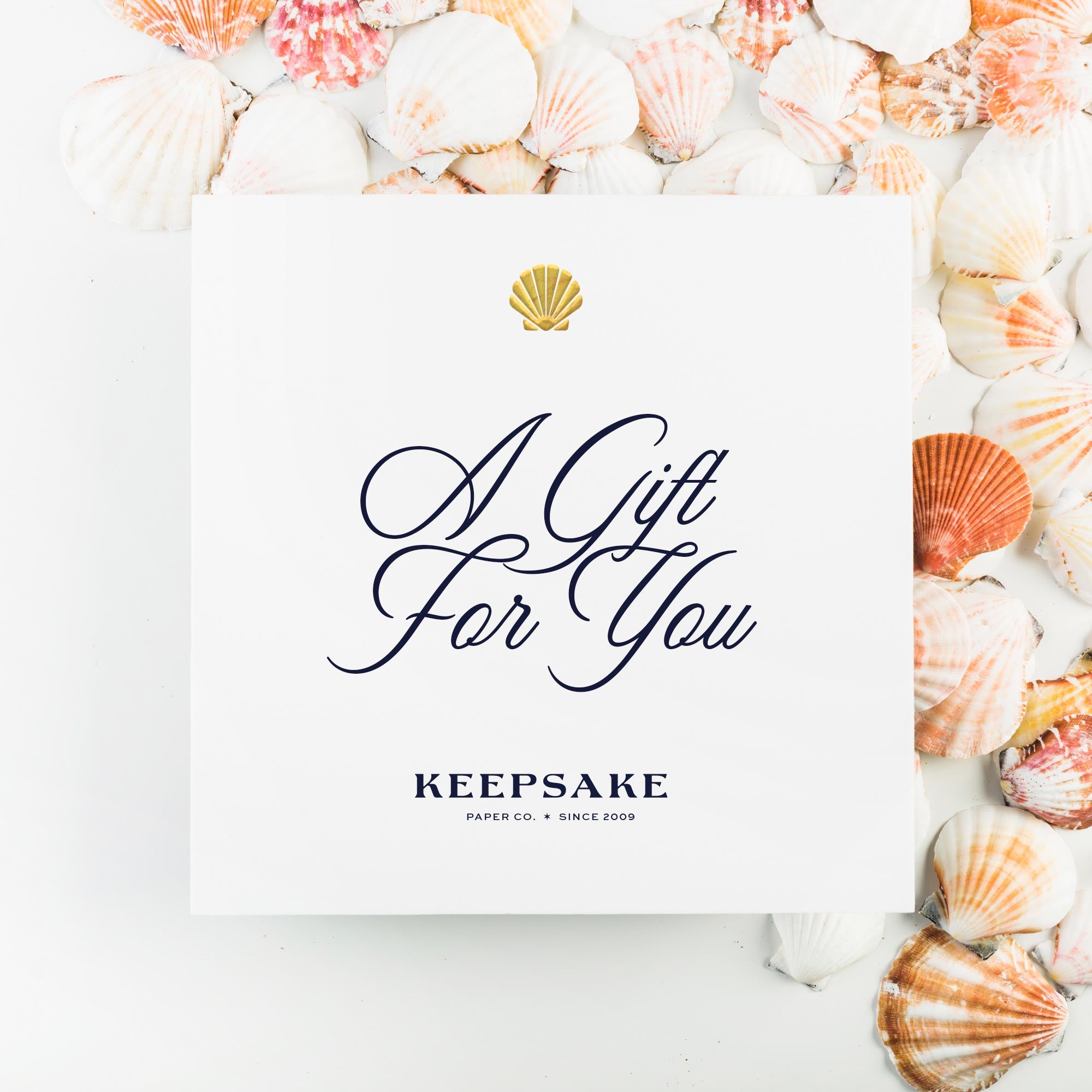 White card sitting atop colorful shells reads "a gift for you" from Keepsake Paper Co.