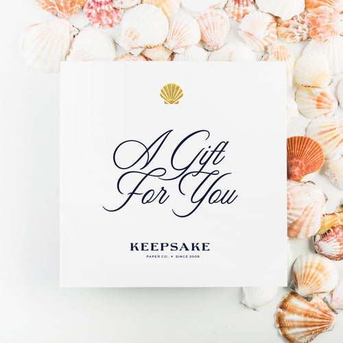 White card sitting atop colorful shells reads "a gift for you" from Keepsake Paper Co.