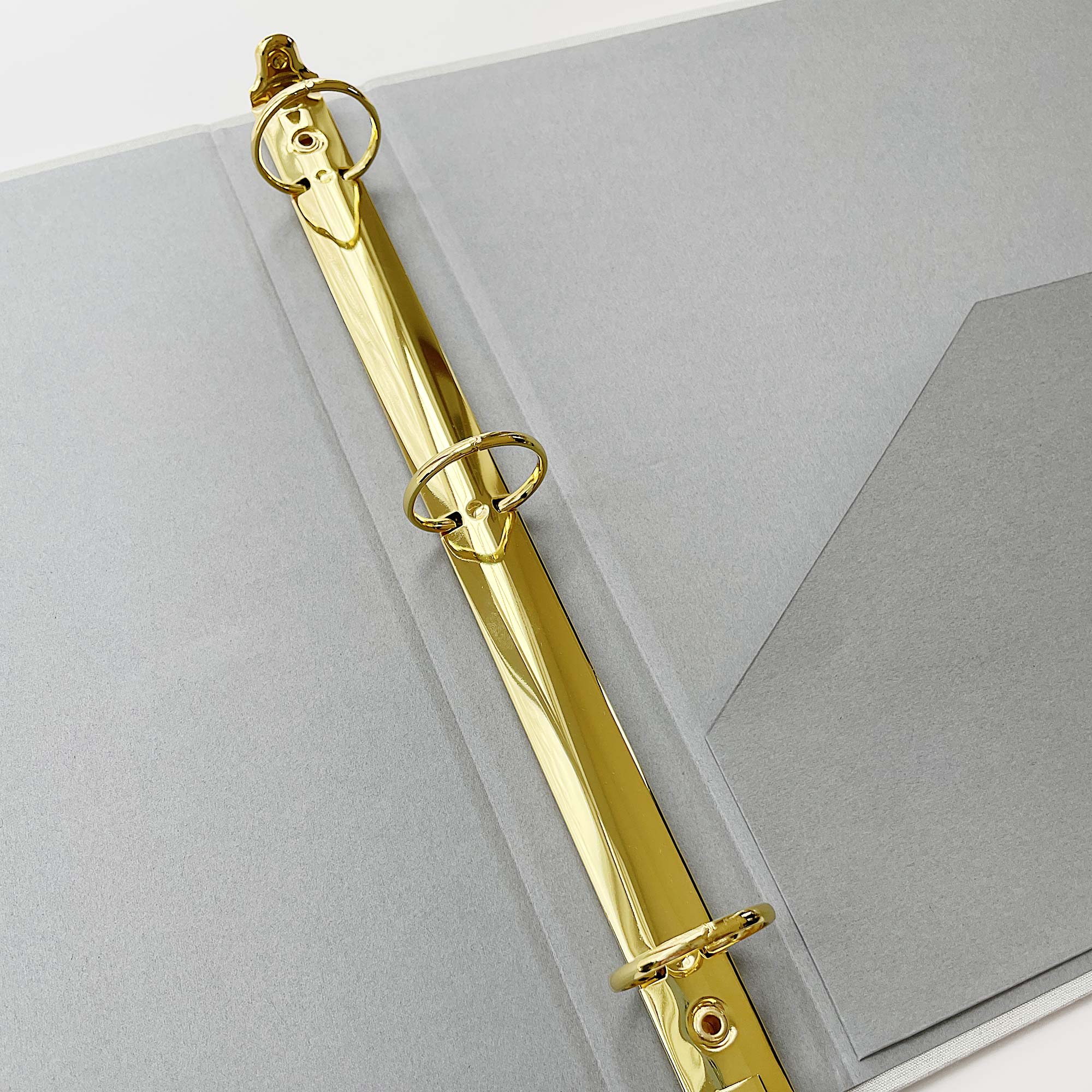 Interior of grey linen binder showing gold 3-ring hardware and a single pocket